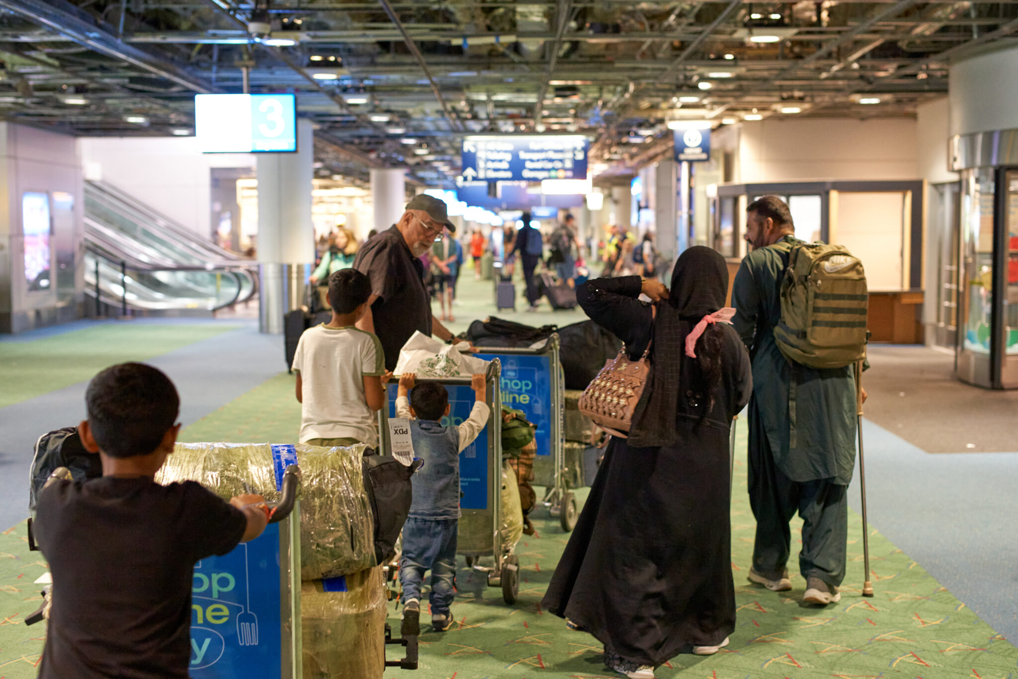 Family of seven with their backs to the camera walking though the airport with their luggage, accompanied by an LCSNW staff member.