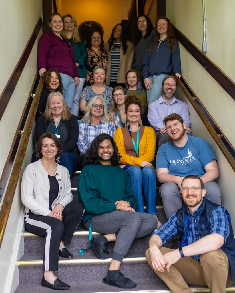 A group of people are sitting throughout a stairwell, grouped together and smiling.