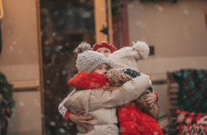 Woman hugging two children wearing winter coats.
